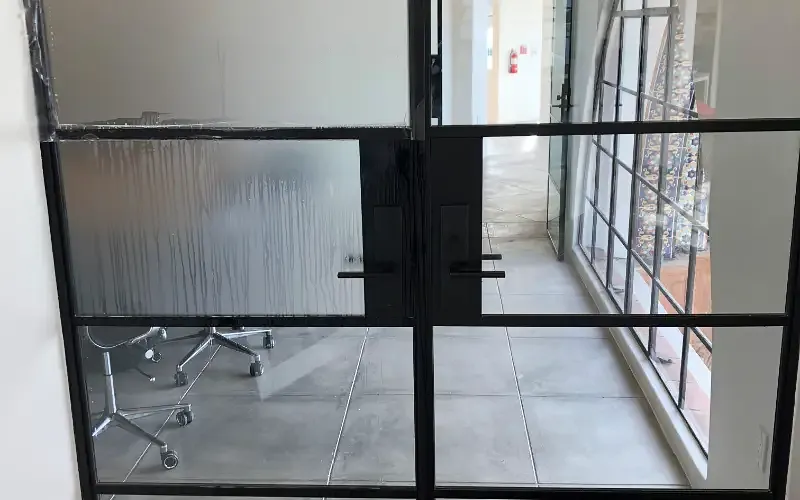 Frosted film being squeegeed onto a steel-framed glass door during installation.