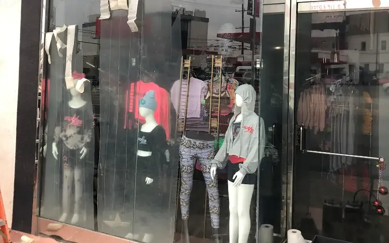 Hazed and scratched storefront glass in front of a clothing display, etched by repeated tagging.